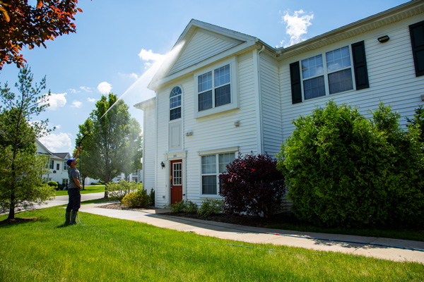 Commercial power washing on apartment building. A Hydro Savage Pressure Washing technician is cleaning vinyl siding with a power washing wand.