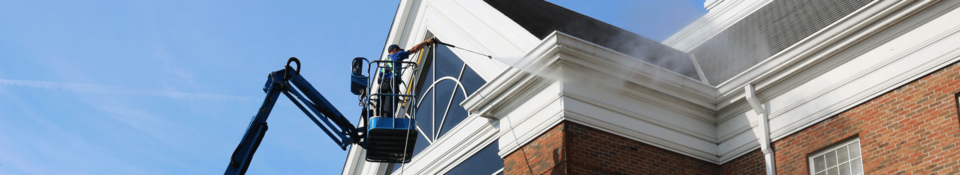 Hydro Savage Pressure Washing employee on a lift power washing the top of a brick commercial building