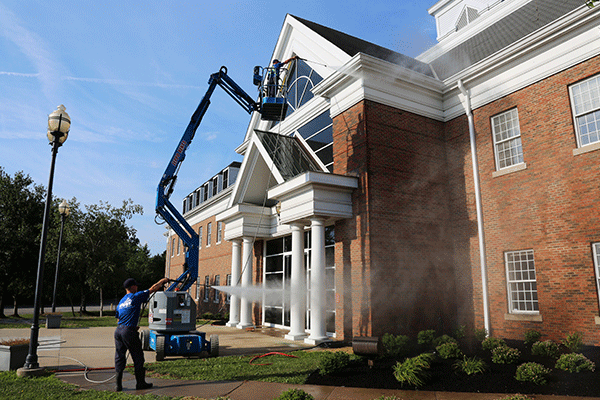 Hydro Savage Pressure Washing employee on a lift power washing the talk of a brick commercial building