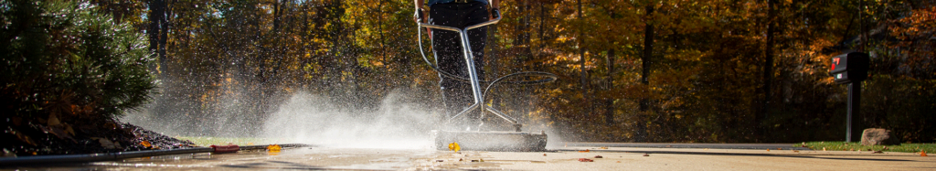 A surface cleaner is being used to power wash a concrete driveway