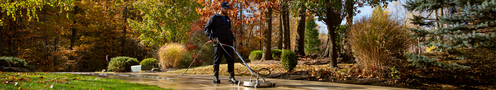 Hydro Savage Pressure Washing technician surface cleaning a concrete driveway during the fall