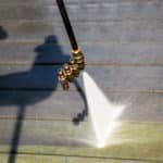 point-of-view of power washing wand cleaning green algae off a dark wooden deck