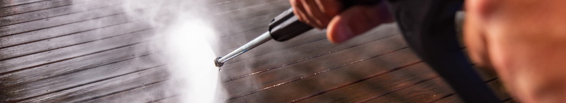 Up-close shot of power washing wand being used to wash floor of a wooden deck