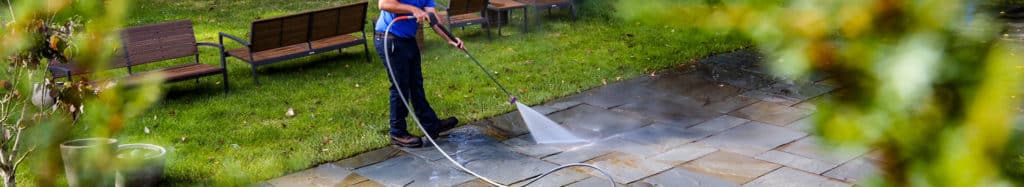 Power washing technician using safe pressure to wash stone back patio with furniture moved to the side