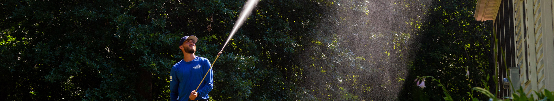 Power washing technician spraying upward while cleaning vinyl siding
