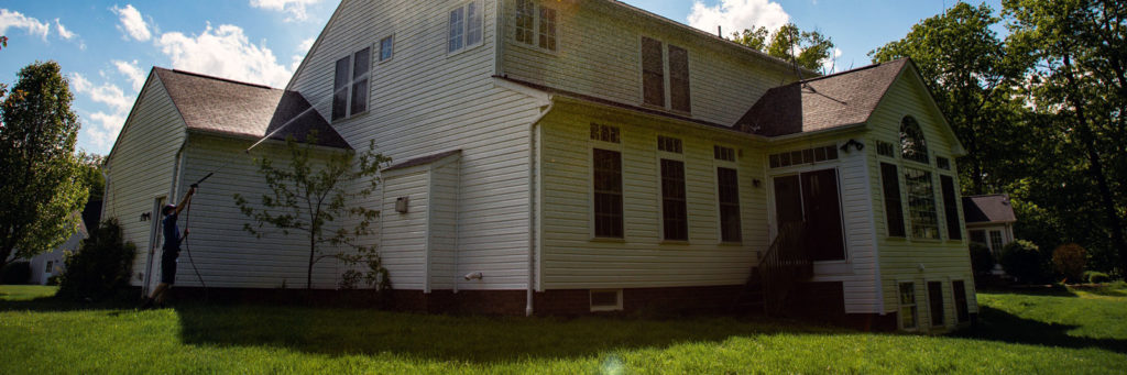 Power washing technician using safe pressure to wash the exterior of a home with yellow vinyl siding