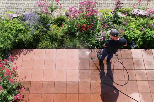 Power washing technician bending over to safely wash a white vinyl fence